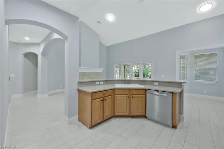 Kitchen featuring light countertops, a sink, stainless steel dishwasher, lofted ceiling, and baseboards