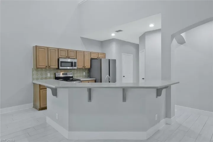 Kitchen with light countertops, a breakfast bar area, stainless steel appliances, backsplash, and visible vents