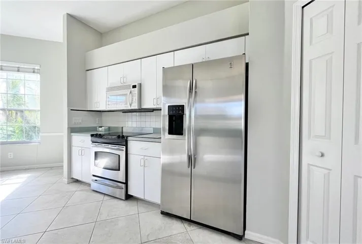 Kitchen featuring backsplash, white cabinetry, stainless steel appliances, and light tile patterned floors