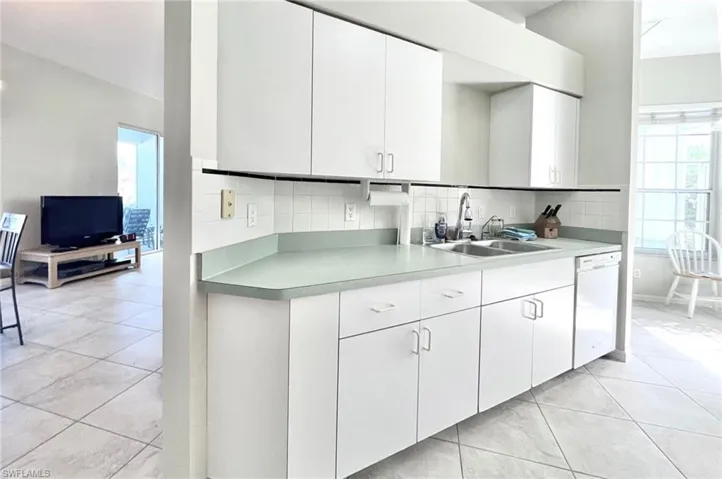 Kitchen with white dishwasher, decorative backsplash, a healthy amount of sunlight, and white cabinets