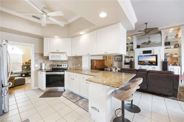 Kitchen with a ceiling fan, white cabinetry, light stone countertops, stainless steel appliances, and a kitchen breakfast bar