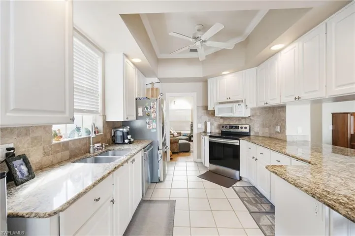 Kitchen featuring white cabinets, light stone counters, stainless steel appliances, ornamental molding, and recessed lighting