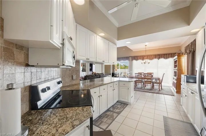 Kitchen with a peninsula, white cabinetry, crown molding, stainless steel appliances, and dark stone counters