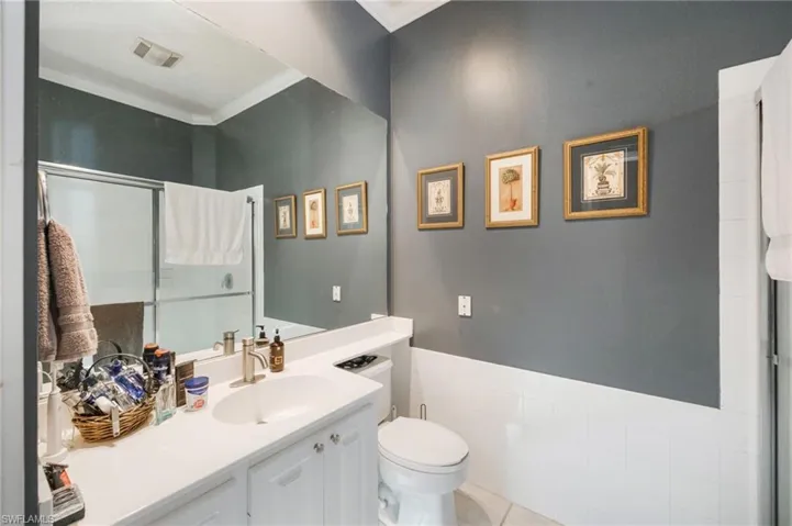 Full bath featuring vanity, tile walls, wainscoting, ornamental molding, and light tile patterned flooring