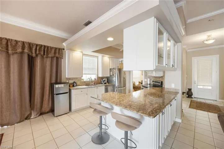 Kitchen with glass fronted cabinets, ornamental molding, dark stone countertops, a peninsula, and stainless steel appliances