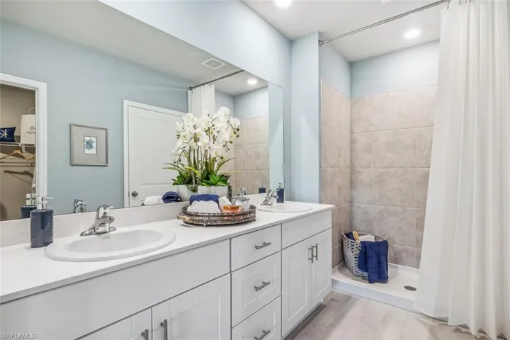 Bathroom with double vanity, tiled shower, wood finished floors, and recessed lighting