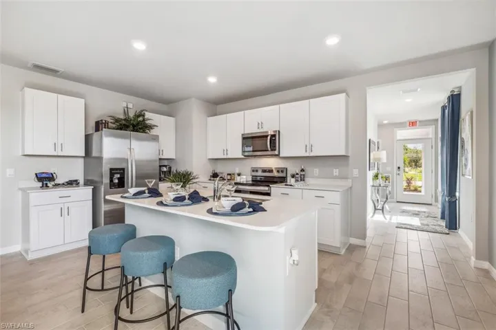 Kitchen with appliances with stainless steel finishes, wood tiled floors, light countertops, white cabinetry, and a kitchen breakfast bar