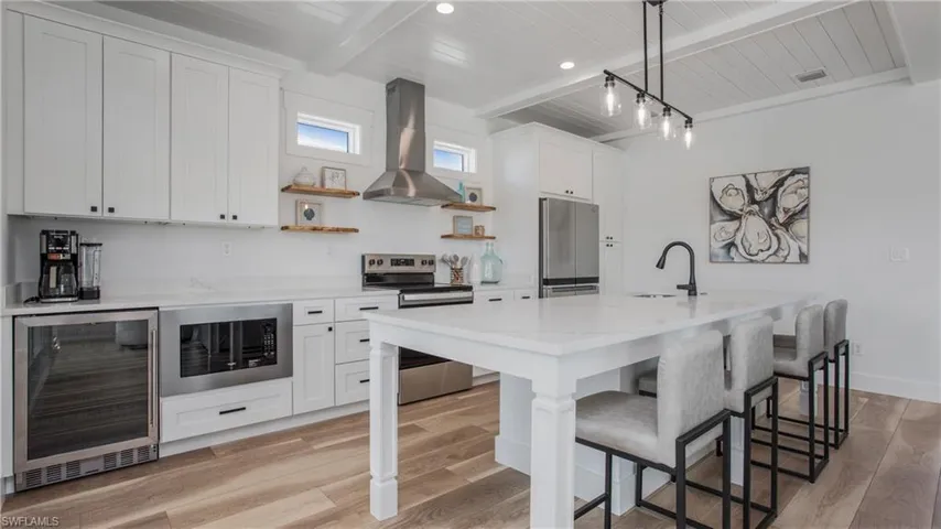 Kitchen with a wood ceiling with exposed beams, beverage cooler, stainless steel appliances, wall chimney range hood, and a breakfast bar