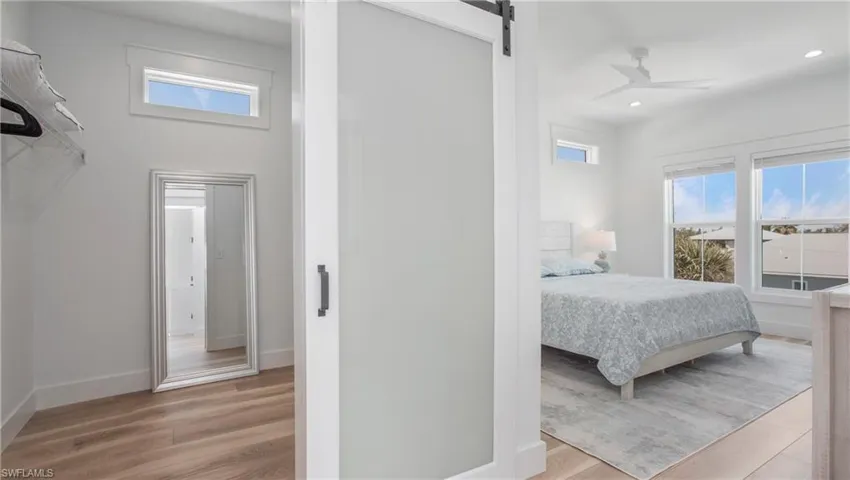 Bedroom with a barn door, multiple windows, light wood finished floors, and recessed lighting