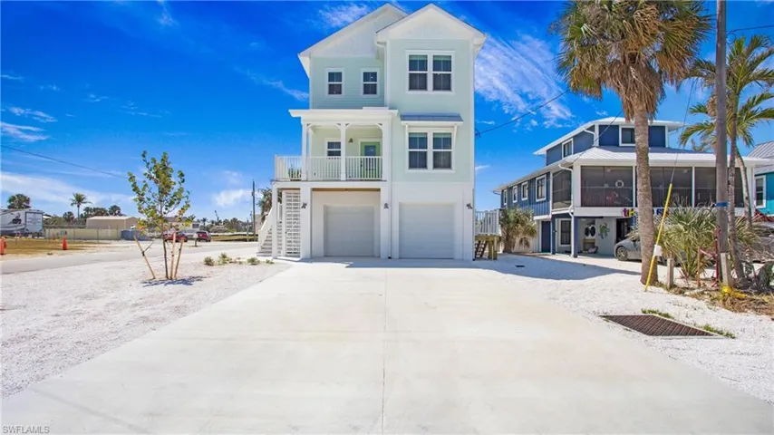 Raised beach house with an attached garage, driveway, stairs, a sunroom, and board and batten siding