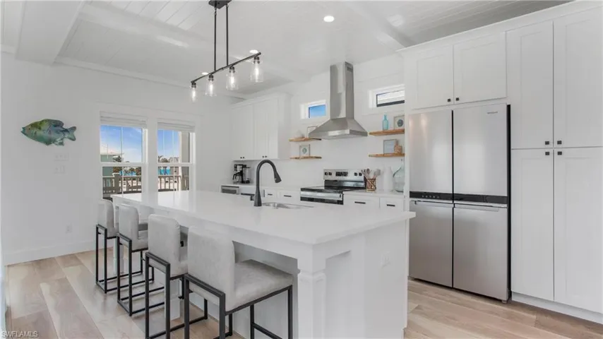 Kitchen featuring stainless steel appliances, a wood ceiling with exposed beams, light wood-type flooring, wall chimney exhaust hood, and white cabinets