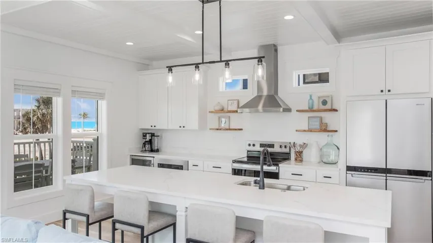 Kitchen with stainless steel appliances, wall chimney exhaust hood, a kitchen bar, open shelves, and recessed lighting