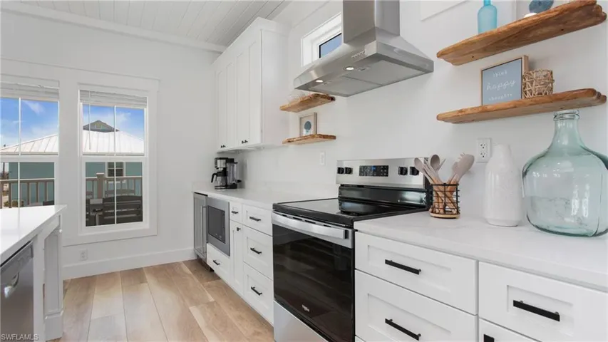 Kitchen featuring open shelves, appliances with stainless steel finishes, wall chimney range hood, light wood-style flooring, and white cabinets