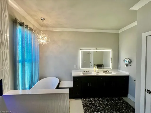 Bathroom featuring a freestanding bath, double vanity, a chandelier, and crown molding