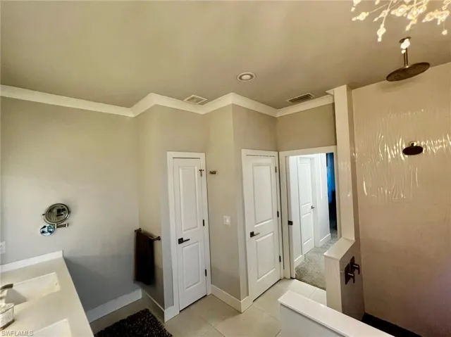 Full bath with light tile patterned flooring, a tile shower, ornamental molding, and double vanity