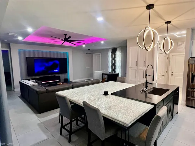 Kitchen featuring a center island with sink, a ceiling fan, open floor plan, stainless steel fridge, and a tray ceiling