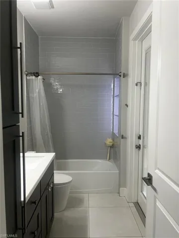Bathroom featuring shower / bath combination with curtain, light tile patterned floors, and vanity