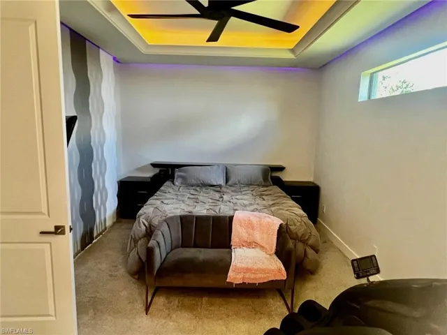Carpeted bedroom featuring a tray ceiling and a ceiling fan