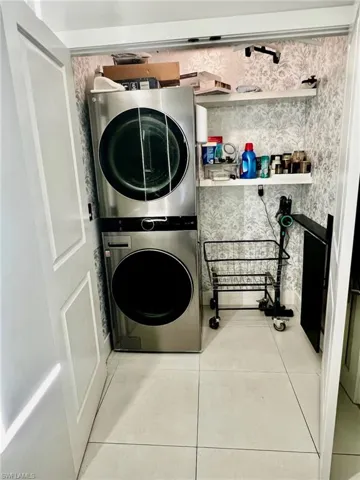 Washroom featuring light tile patterned floors, stacked washer / dryer, and wallpapered walls