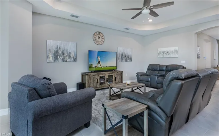 Tiled living room with arched walkways, a tray ceiling, ceiling fan, and recessed lighting