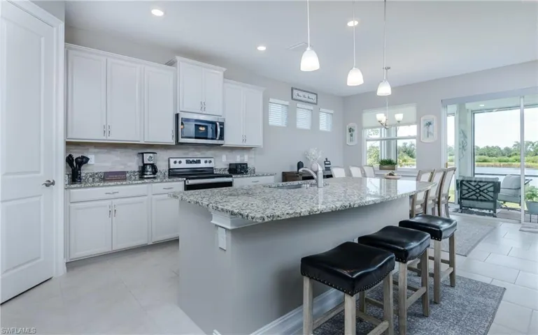 Kitchen featuring decorative backsplash, a breakfast bar area, stainless steel appliances, light stone countertops, and white cabinets
