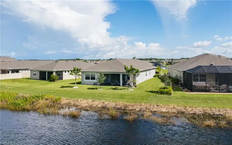Back of house with a water view, a yard, a sunroom, and a lanai