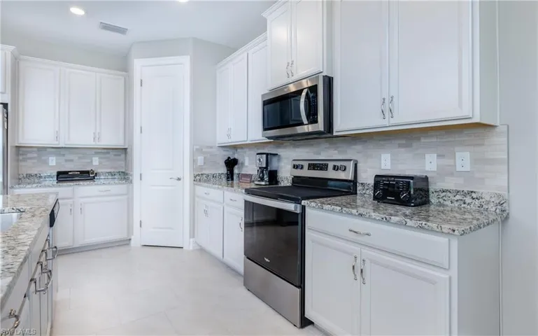 Kitchen with appliances with stainless steel finishes, white cabinetry, decorative backsplash, light stone countertops, and recessed lighting