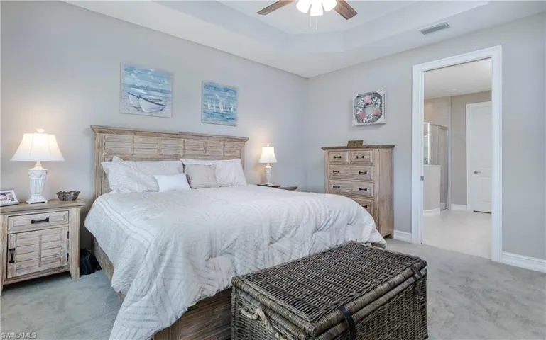Bedroom featuring light colored carpet, a raised ceiling, and a ceiling fan