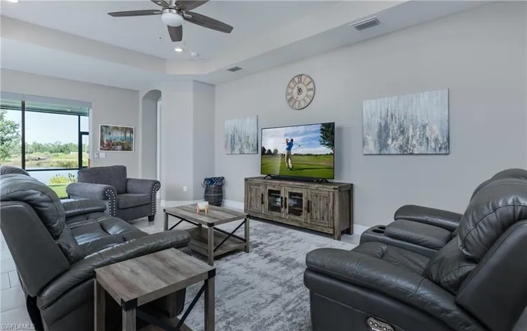 Living room with arched walkways, a tray ceiling, recessed lighting, and ceiling fan