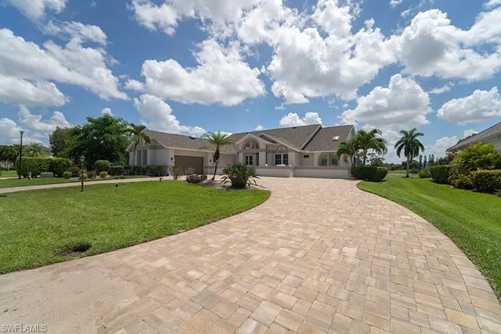 Expansive paver driveway leading to a residence featuring arched windows, a two-car garage, and a light-toned exterior