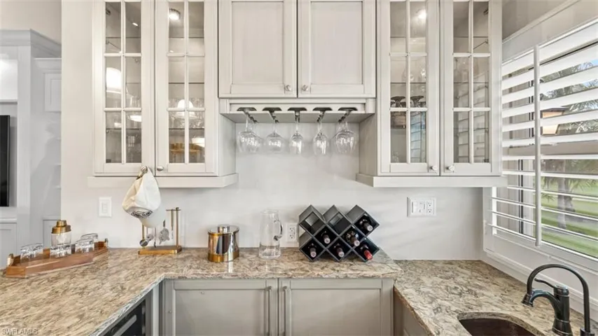 Kitchenette featuring light-toned cabinetry with glass-front uppers, a built-in wine glass rack, and a stone countertop