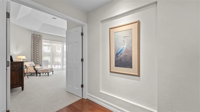 Wood-finish flooring in the entryway leads to a carpeted room featuring a tray ceiling, large sliding glass doors, and patterned drapery
