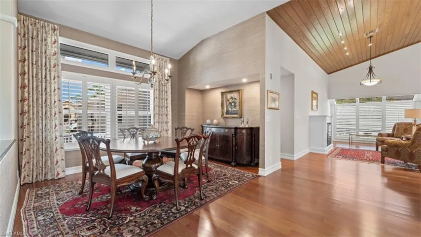 Dining area featuring vaulted ceilings with wood-finish paneling, hardwood flooring, and a chandelier