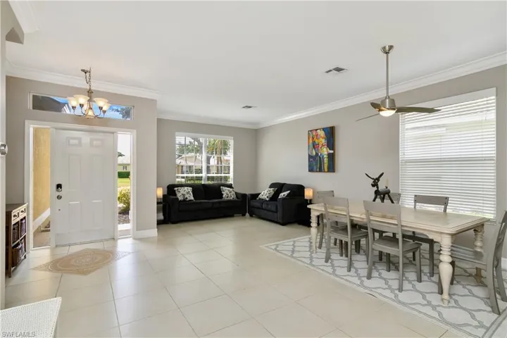 Dining space featuring ornamental molding, light tile floors, and ceiling fan with notable chandelier