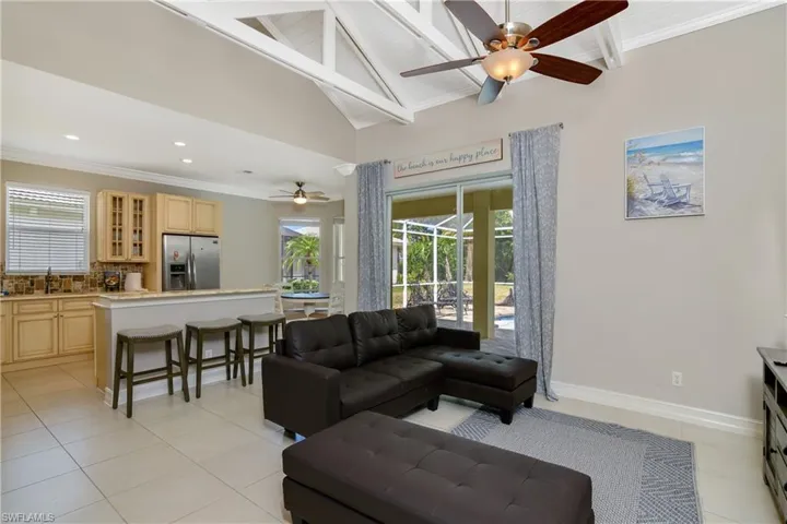 Tiled living room with ceiling fan, beamed ceiling, high vaulted ceiling, sink, and ornamental molding