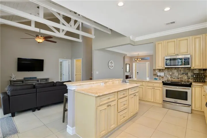 Kitchen featuring ceiling fan, stainless steel appliances, backsplash, light tile floors, and a kitchen bar