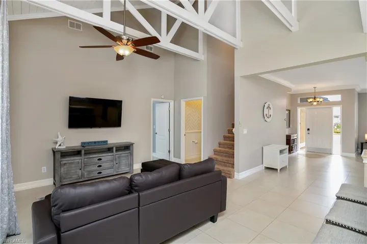 Tiled living room with high vaulted ceiling, beamed ceiling, and ceiling fan with notable chandelier