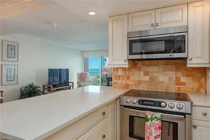 Kitchen with appliances with stainless steel finishes, a peninsula, cream cabinetry, crown molding, and backsplash