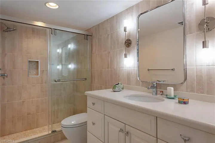 Bathroom featuring vanity, a stall shower, tile walls, and recessed lighting