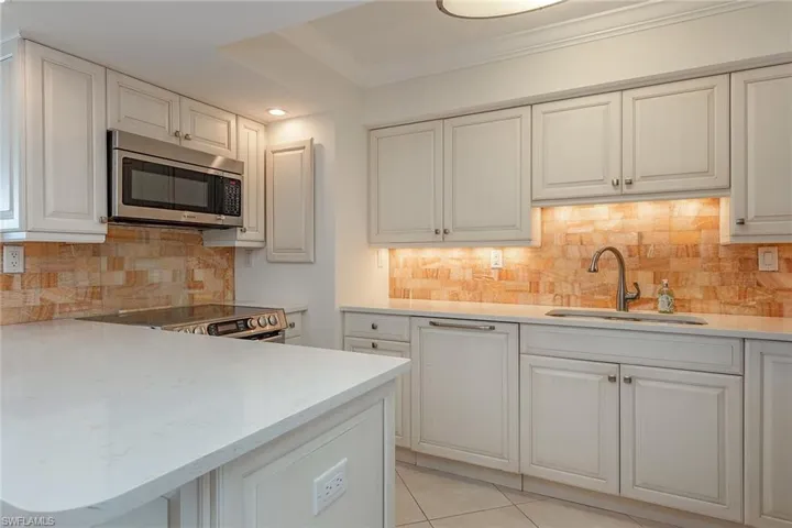 Kitchen with appliances with stainless steel finishes, tasteful backsplash, light stone counters, light tile patterned flooring, and crown molding