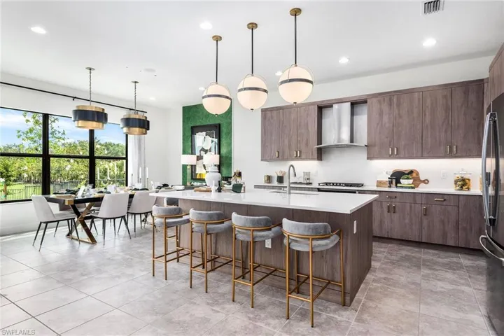 Kitchen featuring wall chimney exhaust hood, sink, dark brown cabinets, an island with sink, and pendant lighting