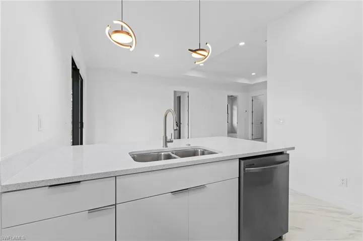 Kitchen with white cabinetry, stainless steel dishwasher, pendant lighting, light stone counters, and light marble finish flooring