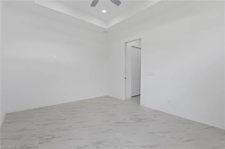 Empty room with a tray ceiling, light marble finish flooring, and recessed lighting