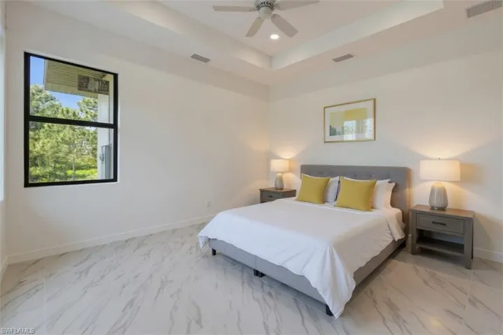 Bedroom featuring a raised ceiling, a ceiling fan, recessed lighting, and light marble finish floors