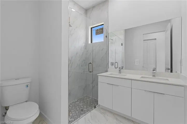 Full bath featuring a marble finish shower, double vanity, and light marble finish floors