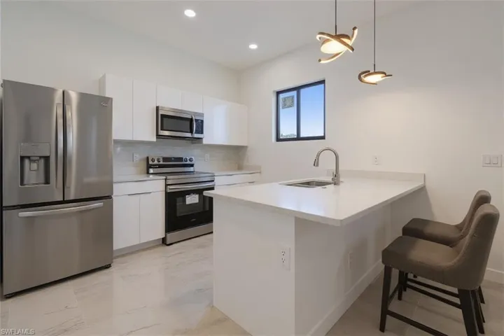 Kitchen with stainless steel appliances, a peninsula, a kitchen breakfast bar, white cabinets, and pendant lighting