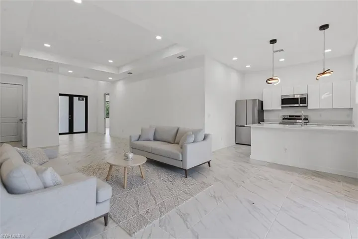Living room with recessed lighting, light marble finish floors, a raised ceiling, and french doors