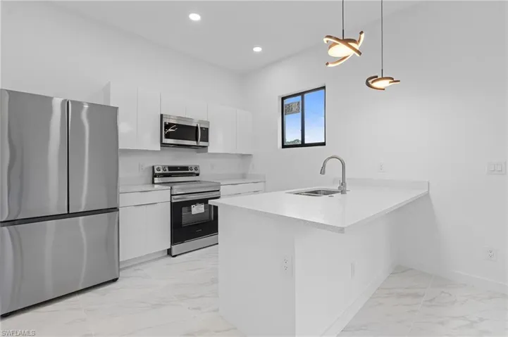 Kitchen with stainless steel appliances, light marble finish flooring, a peninsula, decorative light fixtures, and white cabinetry