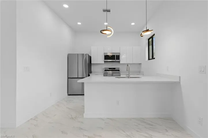 Kitchen with stainless steel appliances, a peninsula, white cabinets, hanging light fixtures, and light marble finish floors