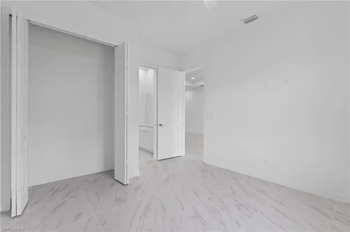Unfurnished bedroom with ceiling fan, light marble finish flooring, ensuite bathroom, and a closet